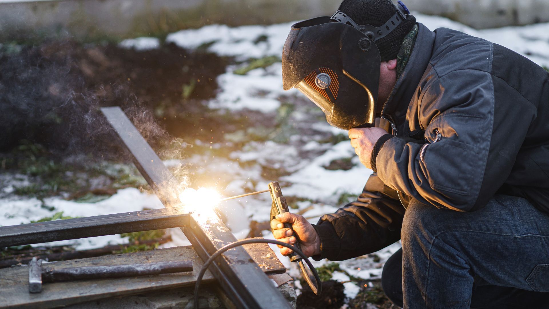 A man wearing a welding mask is welding a piece of metal.