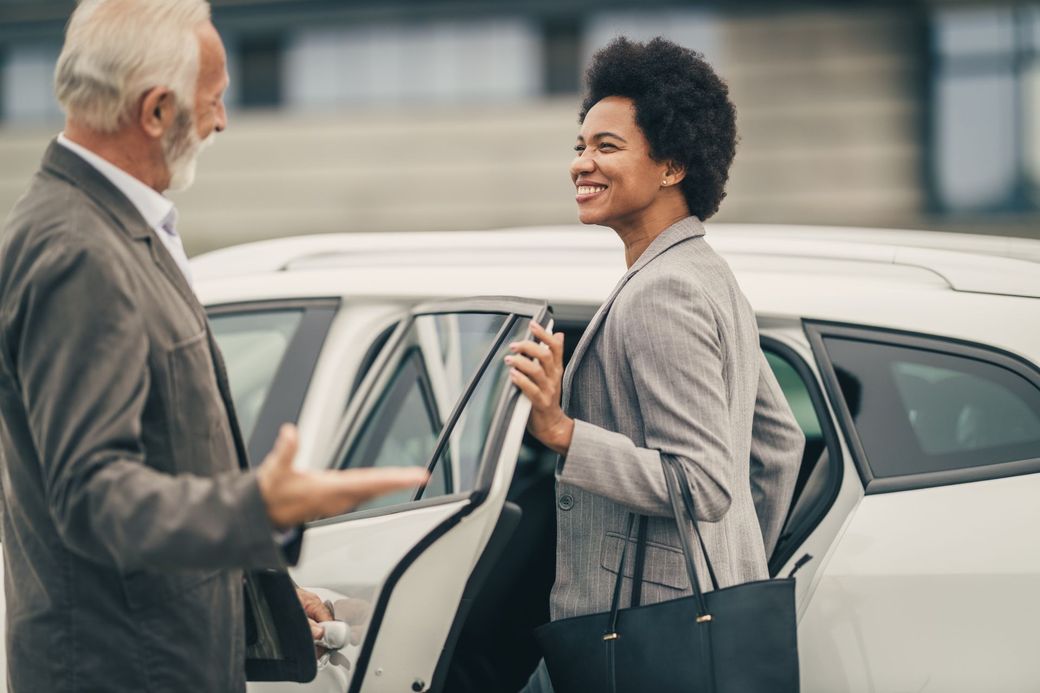 A woman is sitting in the driver 's seat of a car being handed a napkin.