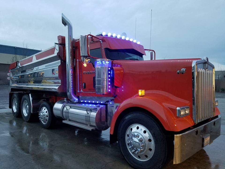 Red dump truck with chrome accents and blue lights under a cloudy sky.