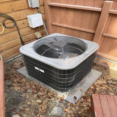 An air conditioner is sitting on the ground next to a wooden fence.