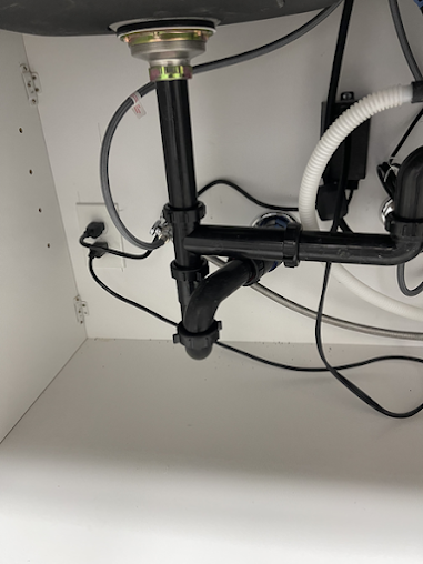 A sink underneath a cabinet with a lot of wires coming out of it.