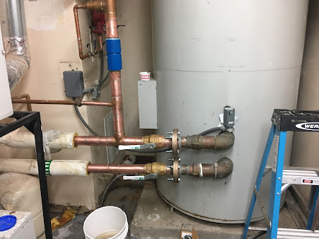 A water heater is sitting in a room next to a ladder.