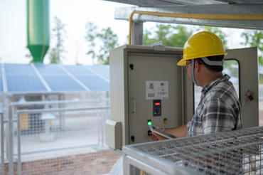 Technician in yellow hard hat operates control panel near solar panels.
