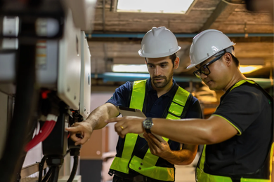 Two engineers in hard hats and safety vests inspecting machinery.