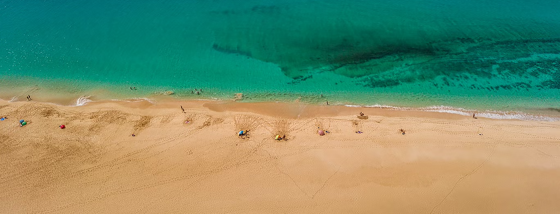 An aerial view of a sandy beach surrounded by turquoise water.