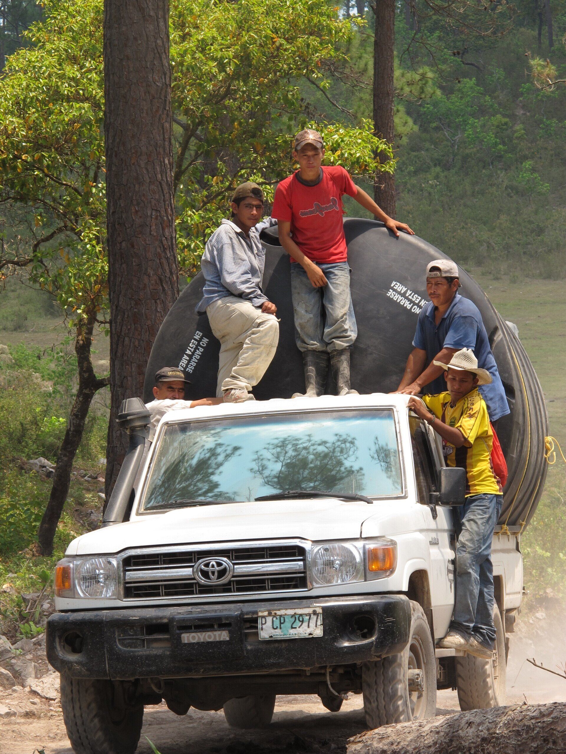 Hondurans using a pick-up truck to transport a big piece of equipment.
