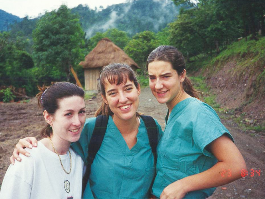 Three team member pose for the camera in a village.