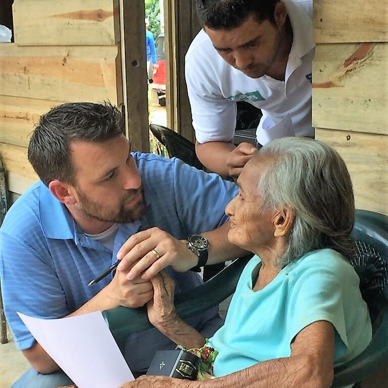 At a house dedication, a team member holds the hand of and talks with an elder and a translator.