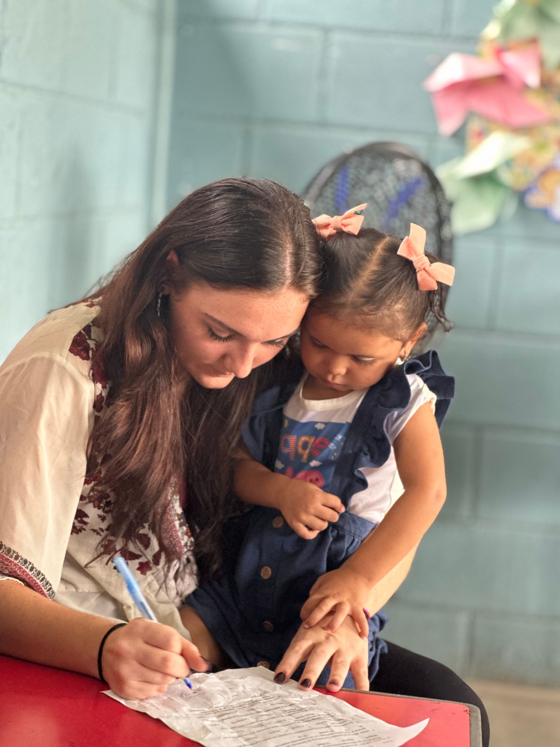 A team member and a little girl focus on some work at a table.