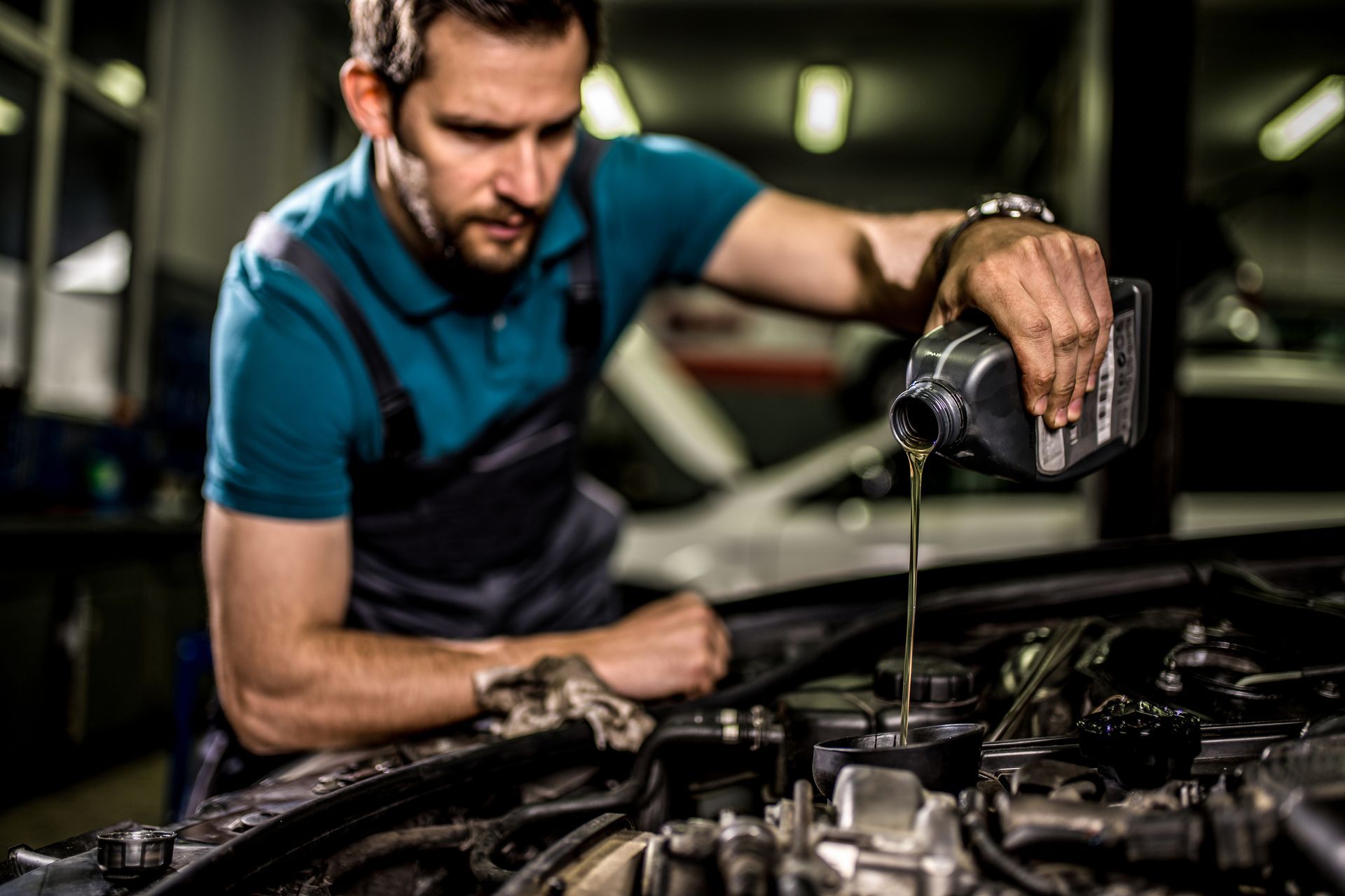 Mechanic pouring oil into a car engine in a garage.