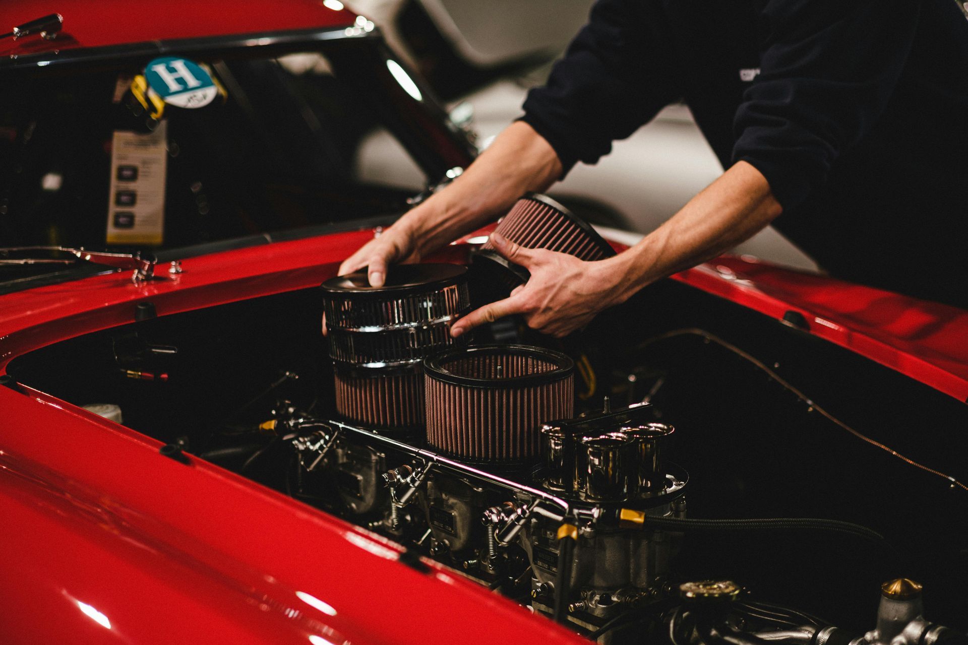 Person working on a red classic car engine, with air filters.