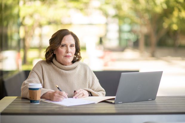 A woman is sitting at a table with a laptop and a cup of coffee.