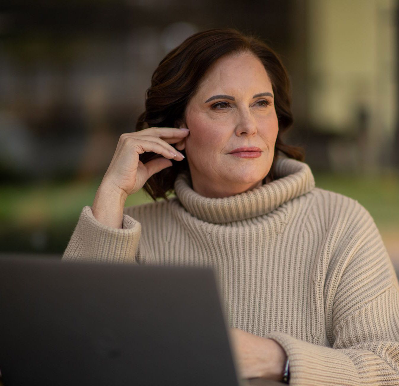 A woman in a sweater is sitting in front of a laptop computer.