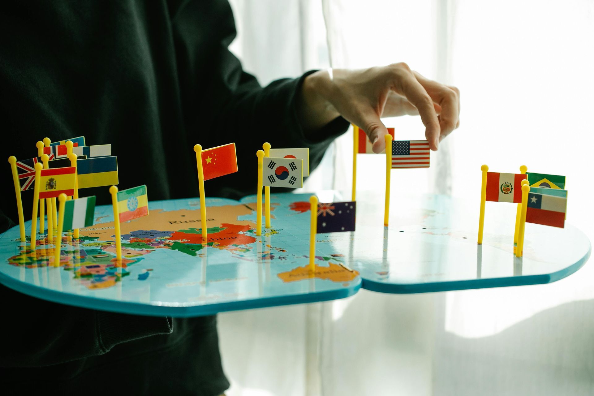 A person is holding a map of the world with flags on it.