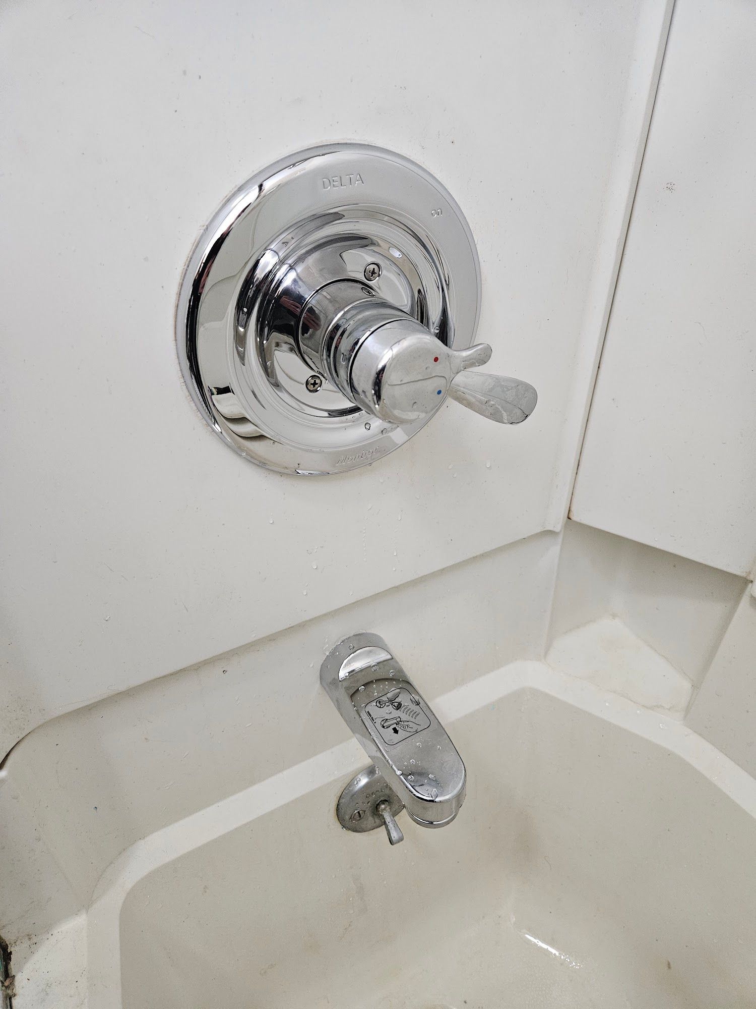 A chrome shower faucet handle and spout mounted on a white shower wall.