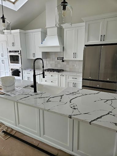 A modern kitchen featuring white cabinets, stainless steel appliances, and a white marble countertop with black veining.