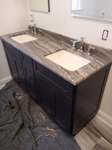 A double-sink bathroom vanity with dark blue cabinets, a grey-veined stone countertop, and chrome faucets.
