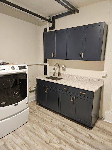A laundry room featuring a white washing machine, dark gray cabinets, a light-colored countertop, and a stainless sink.