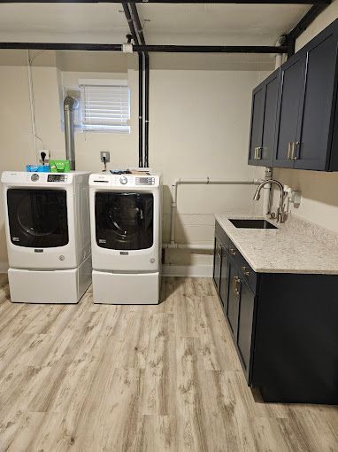 A laundry room with two white front-load appliances next to dark cabinets, a sink, and a light countertop.