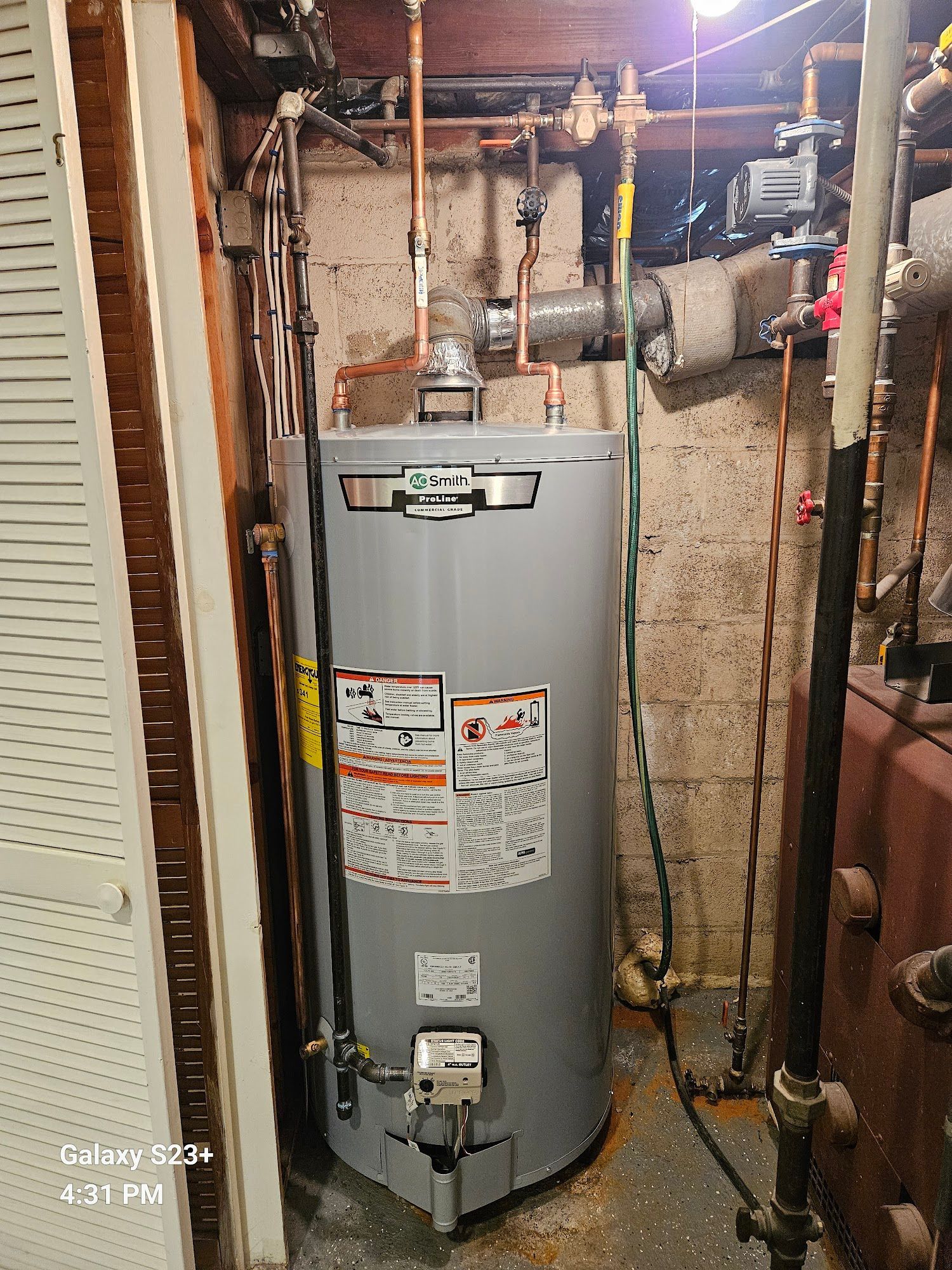 A grey residential water heater with copper plumbing connections in a basement utility area.