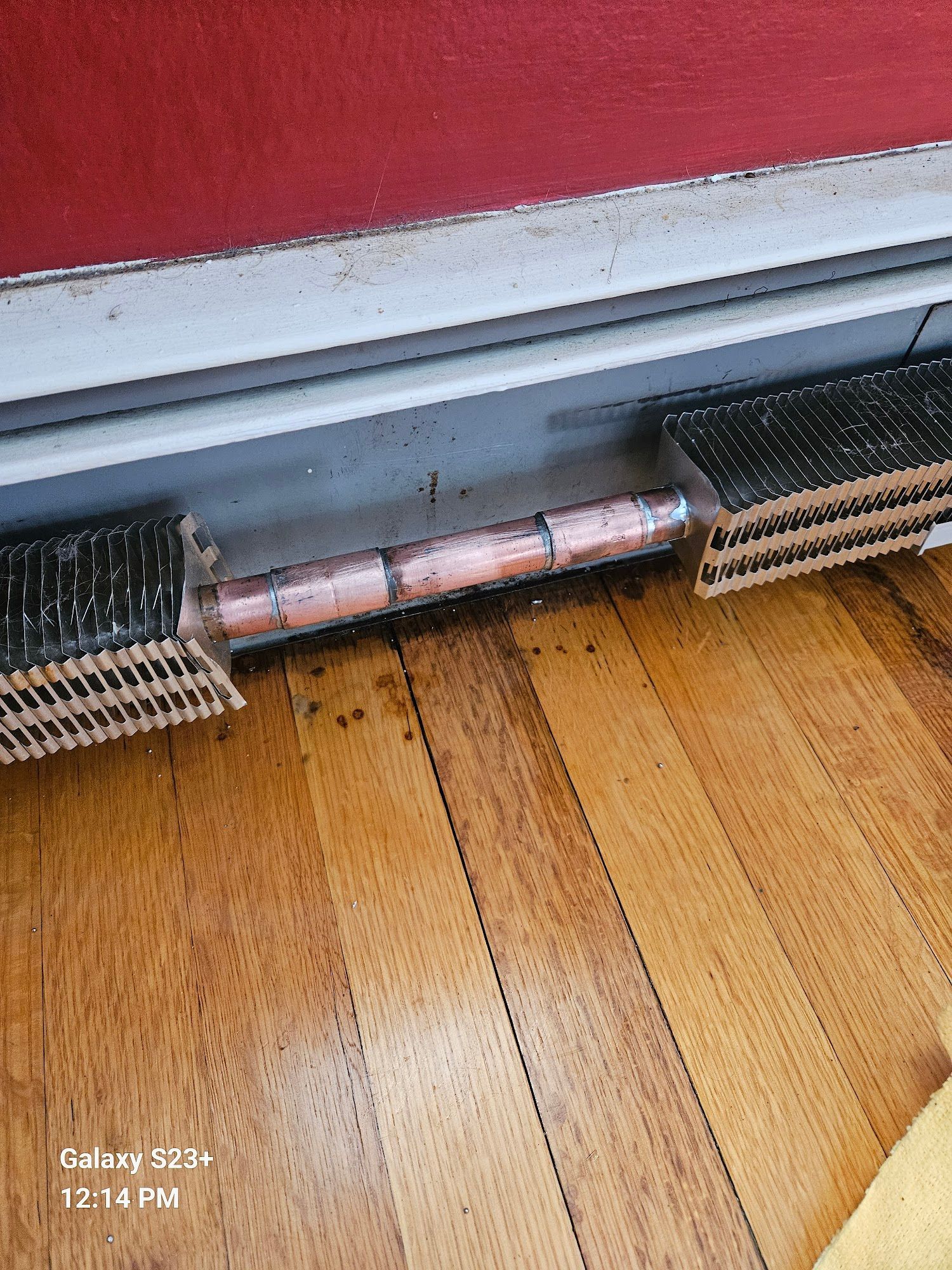 A section of a residential baseboard heater with the metal cover removed, exposing the copper heating pipes.
