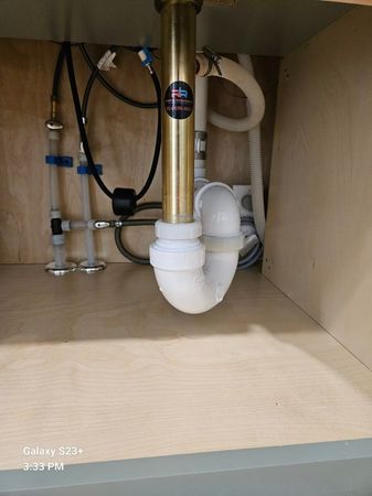 Water flows from a wall-mounted gold faucet into a clean white sink with a matching gold drain cover.