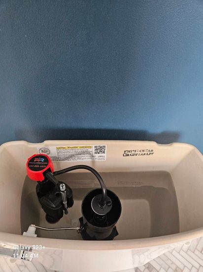 A gloved hand holds a disassembled sink drain pipe assembly filled with accumulated hair and debris under a kitchen sink.