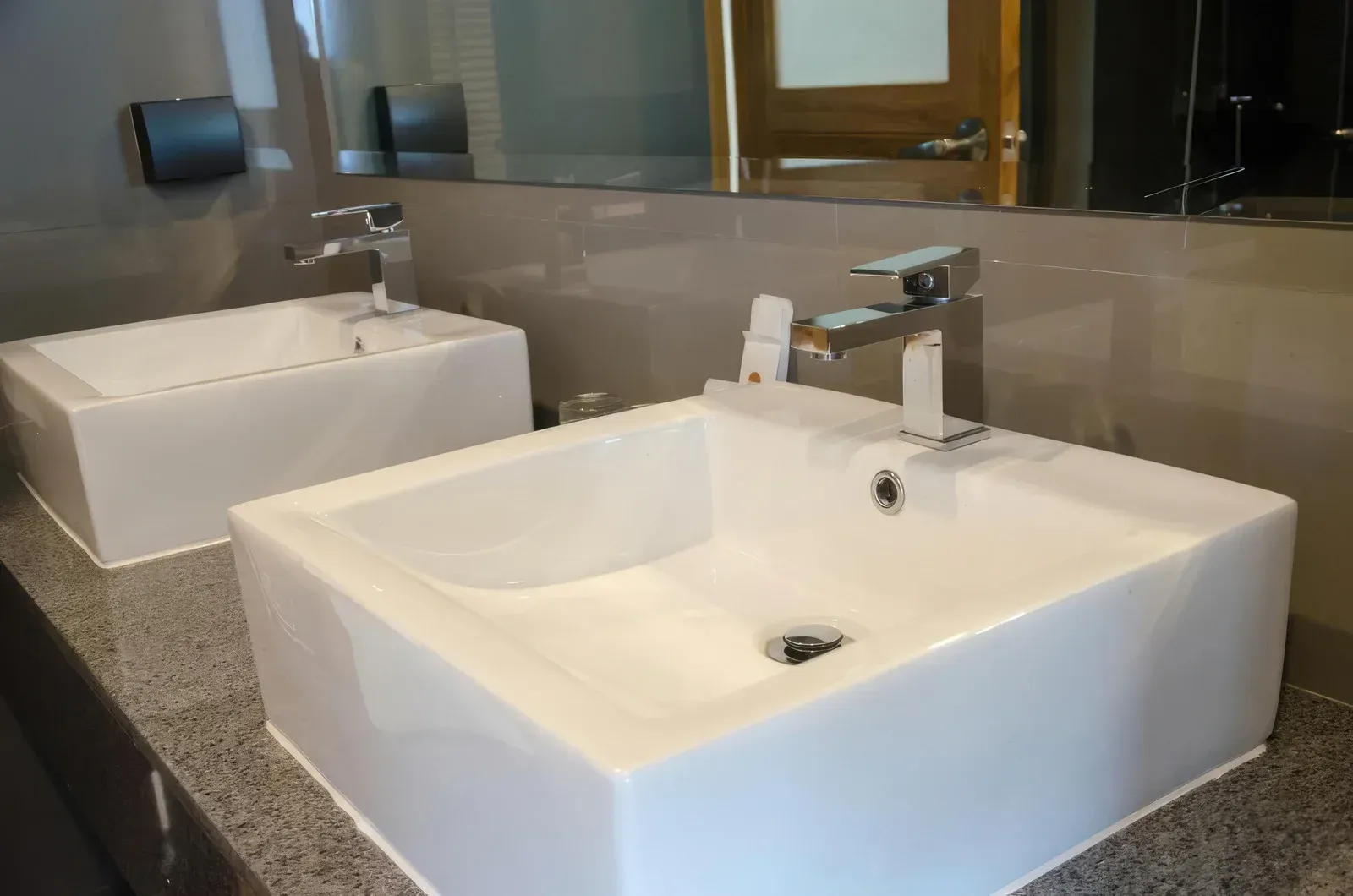 A professional wearing a cap and gloves inspects under-sink plumbing while holding a clipboard.
