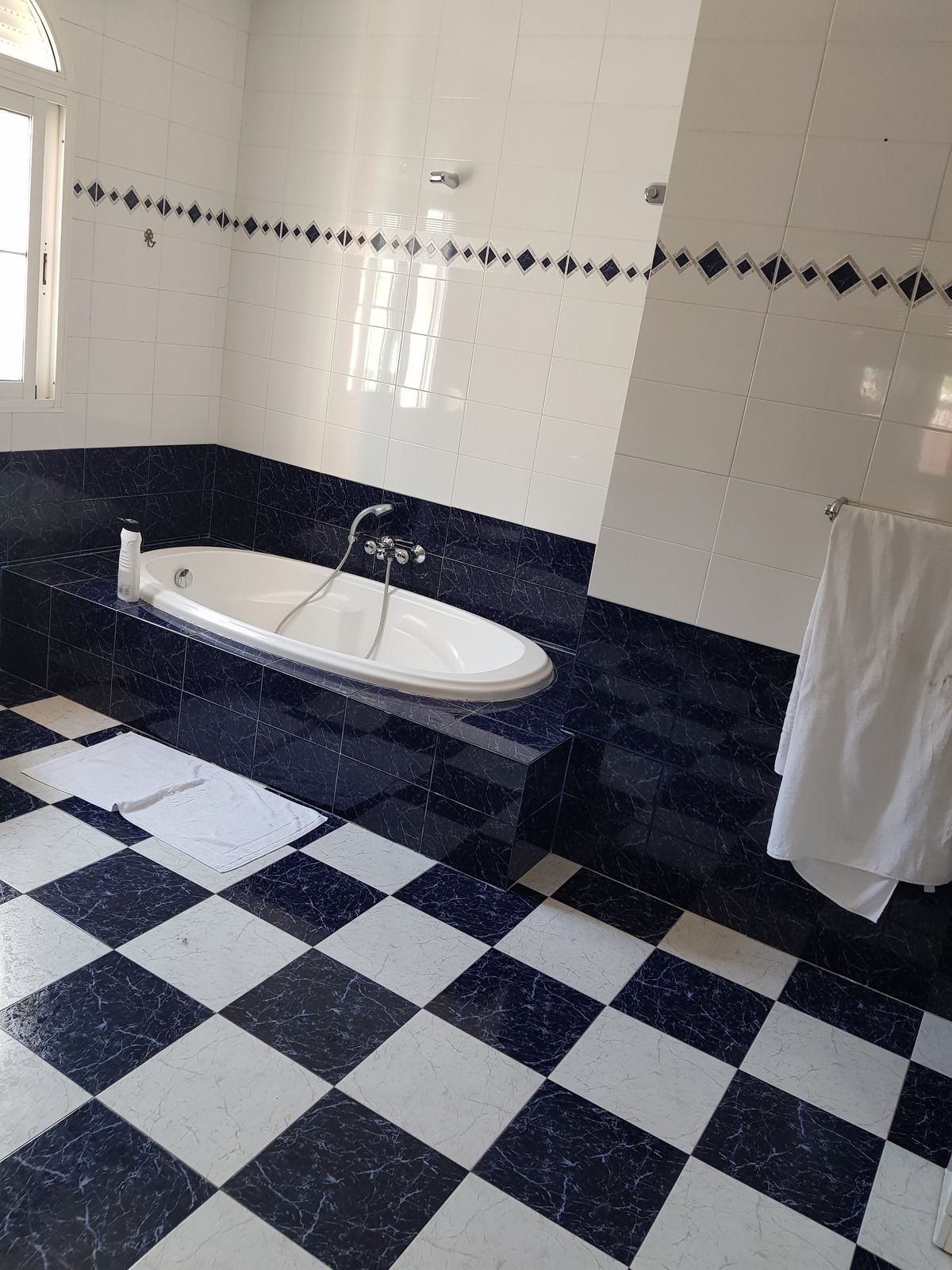 A bathroom featuring a white bathtub set into a blue and white checkered tiled platform and floor.