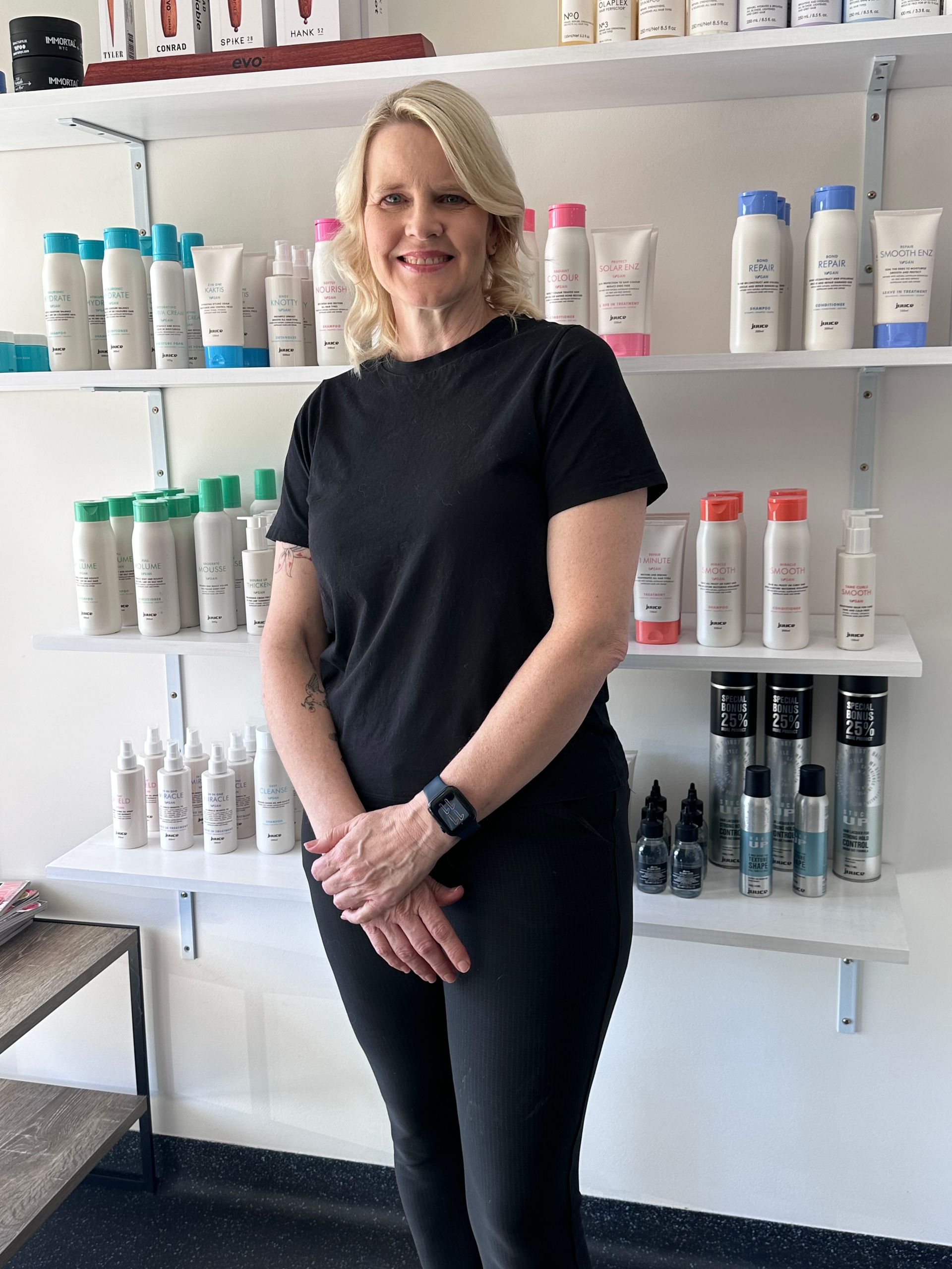 Hair Salon Owner Lady Standing In Front Of Hair Products In A Salon — Haelo Hair In Bomaderry, NSW