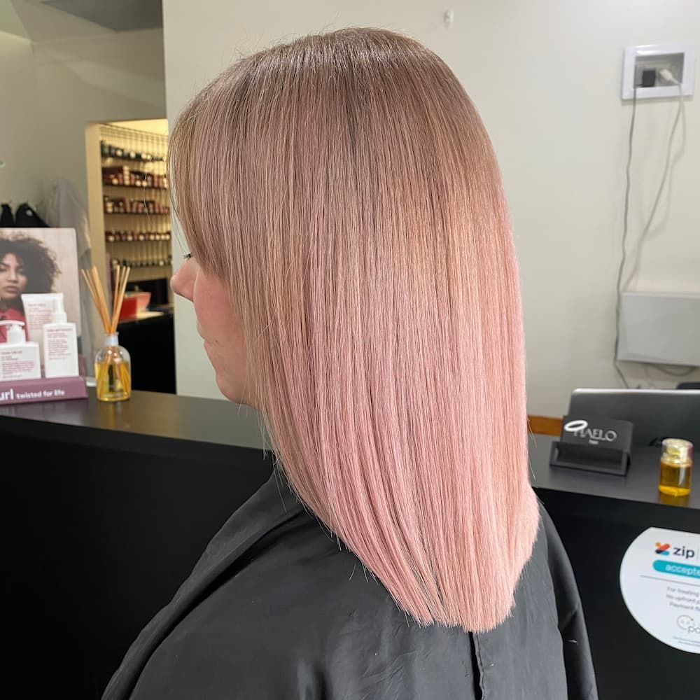 A Woman With Pink Hair Is Sitting At A Counter In A Salon — Haelo Hair In Bomaderry, NSW