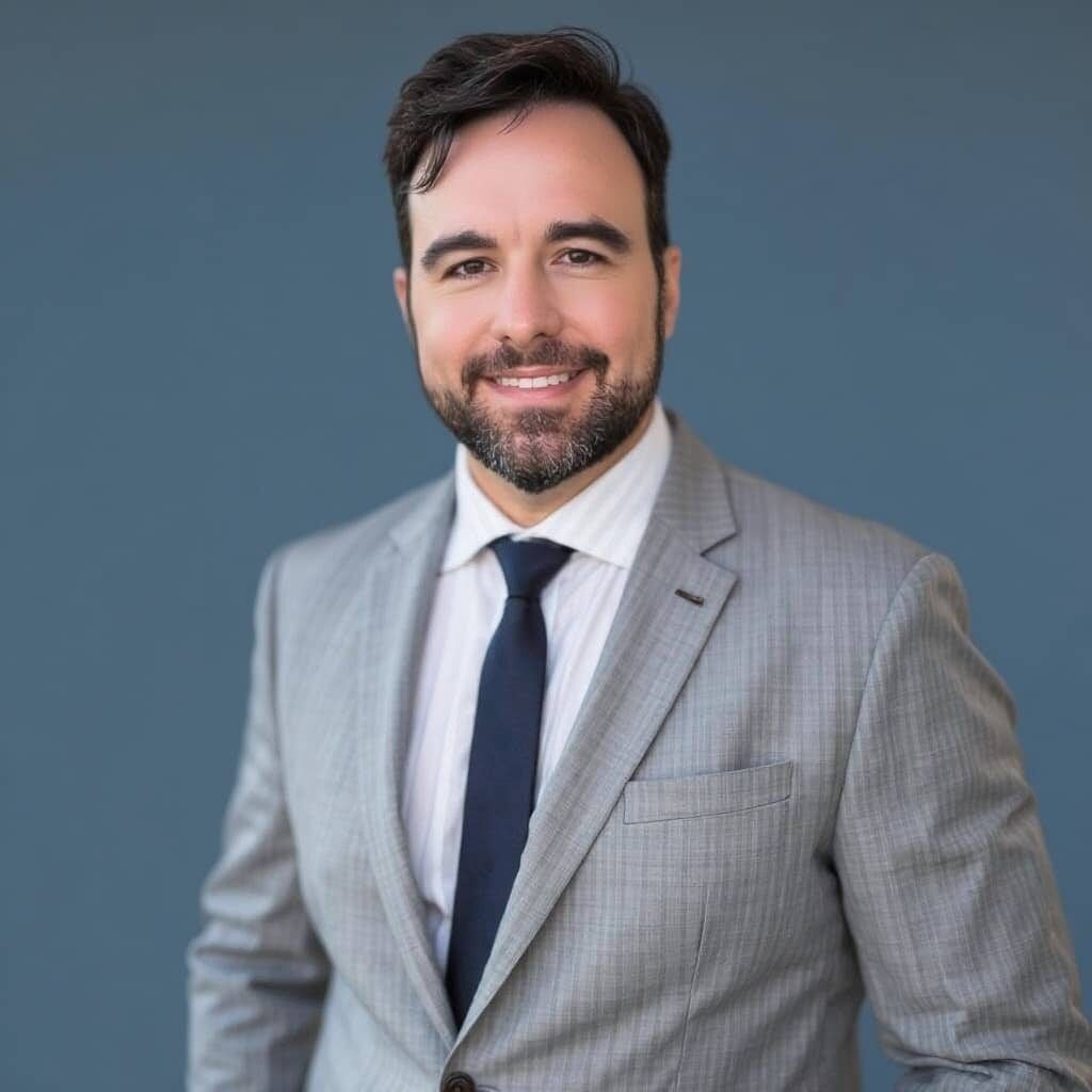 Man in gray suit, blue tie, smiling against a blue background.