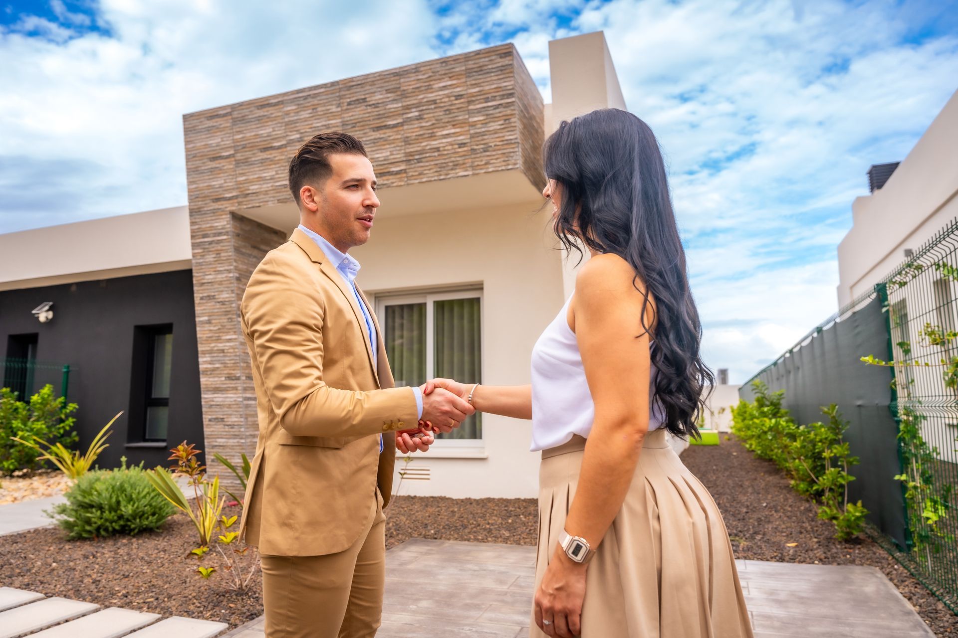 A real estate agent shakes hands with a woman in front of a modern house.