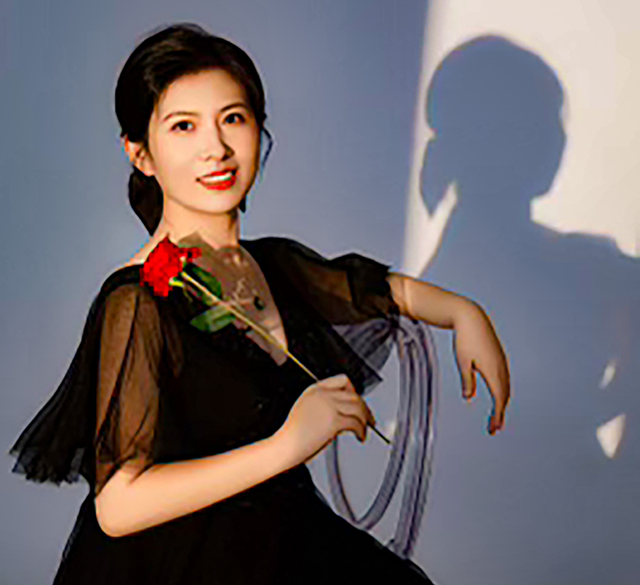 A woman in a black dress is sitting in a chair holding a red rose.