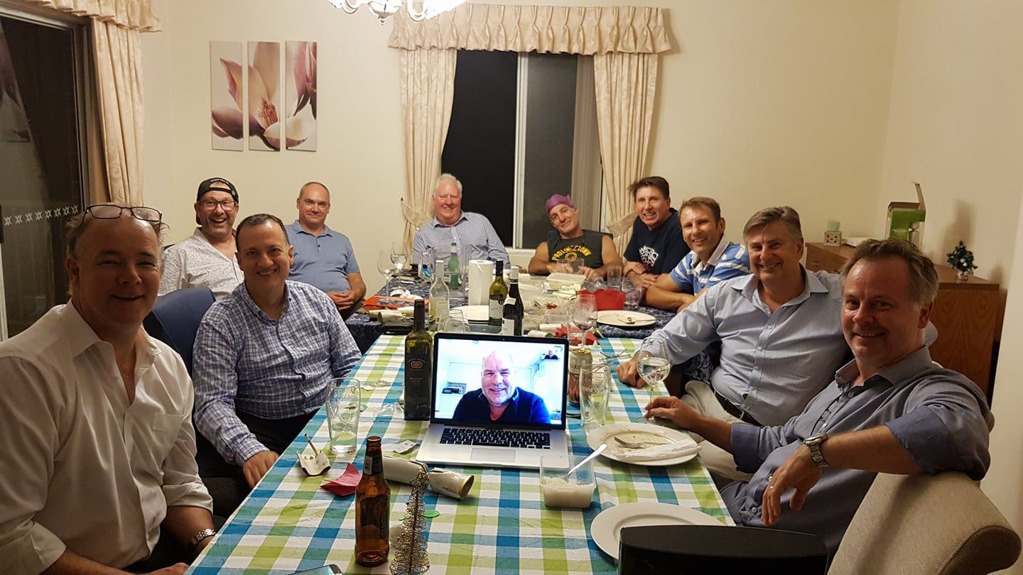 A group of men are sitting around a table with a laptop on it.