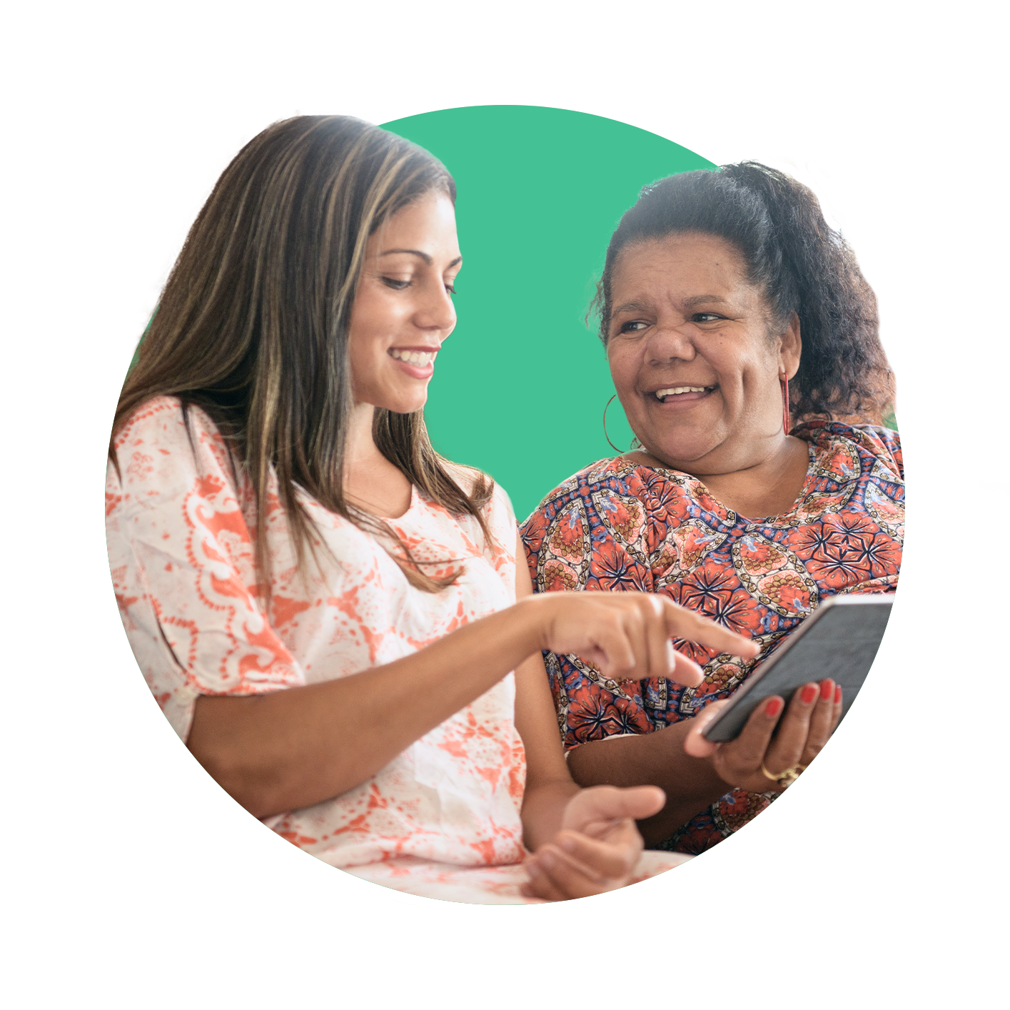 Two First Nations women conversing, with one talking and pointing at her notebook, whilst the other is smiling and looking towards her peer