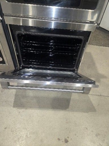 Stainless steel oven door open, showing interior and racks.