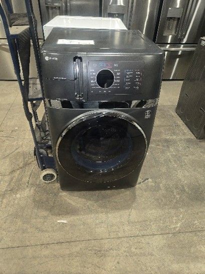 A dark, damaged washing machine on a hand truck, indoors on a concrete floor.