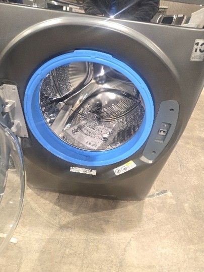 Front-load washing machine with a blue door ring, in a room with a concrete floor.