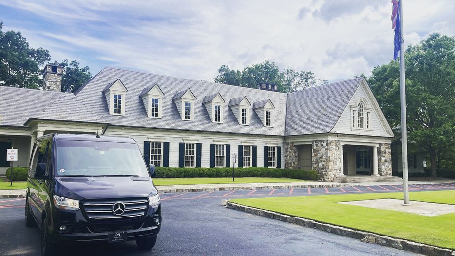 A black van is parked in front of a large house.