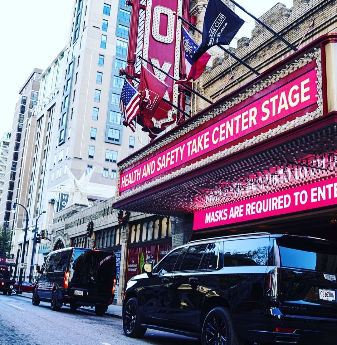 Cars are parked in front of a theater that says masks are required to enter