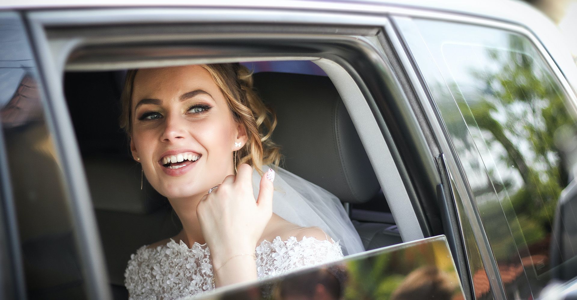 A bride in a wedding dress is sitting in a car and smiling.