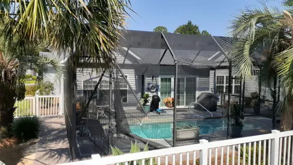 Screened-in porch on ground level with balcony above; beige siding, tan railing, door, windows, and light gravel.