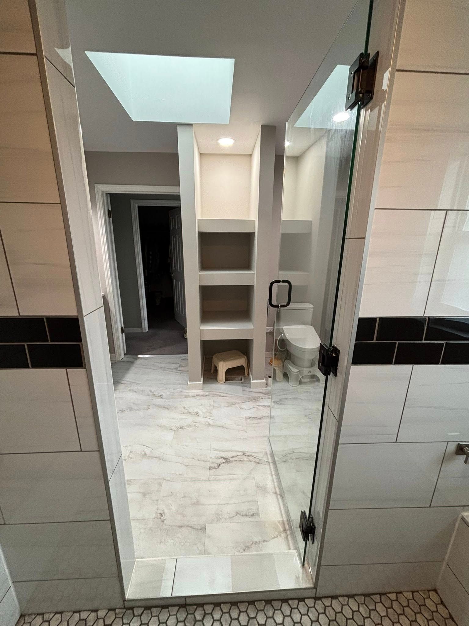 Modern bathroom with glass shower door, built-in shelves, and pebble floor.