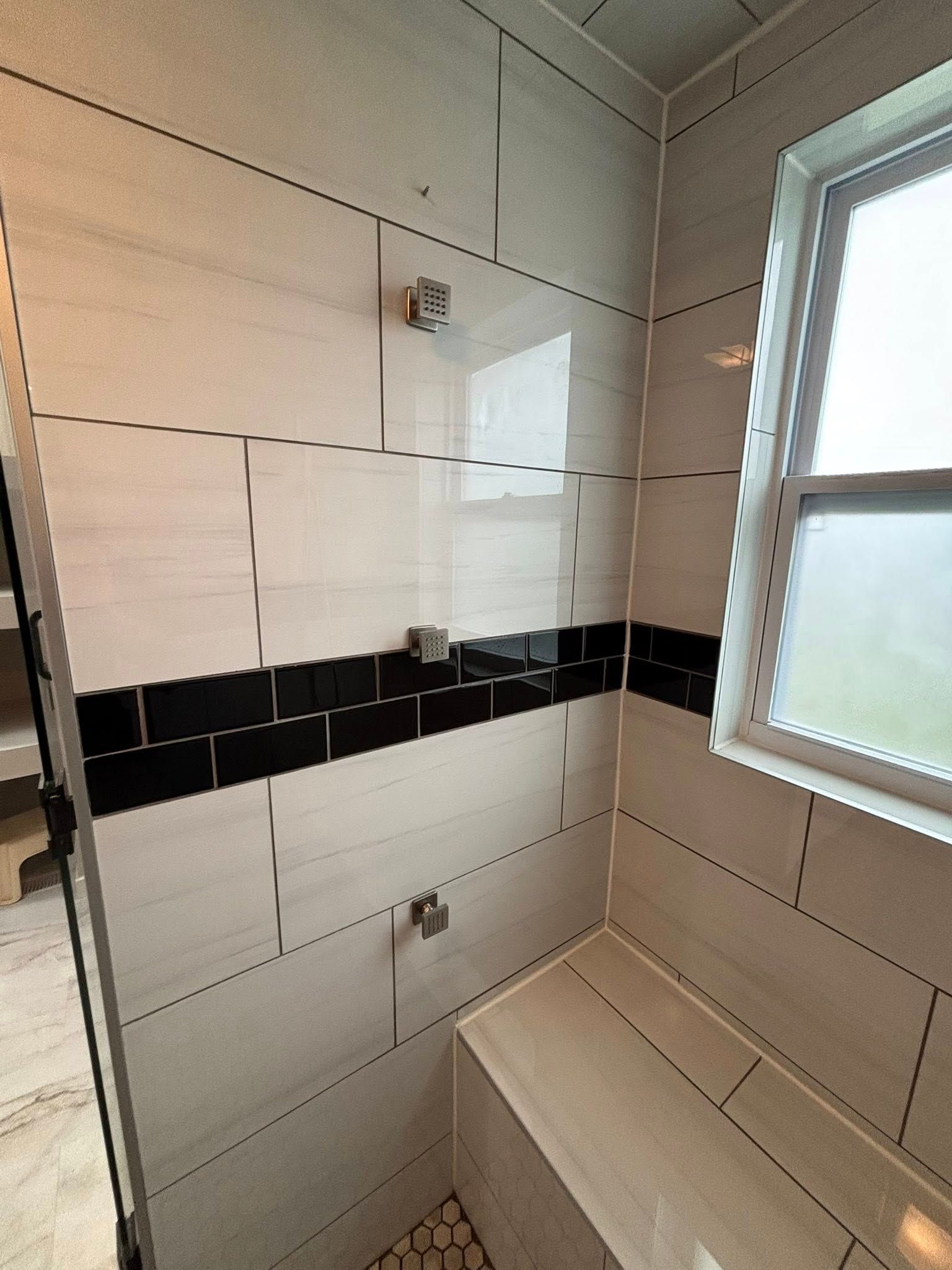Shower with white and black tile, bench, and window.