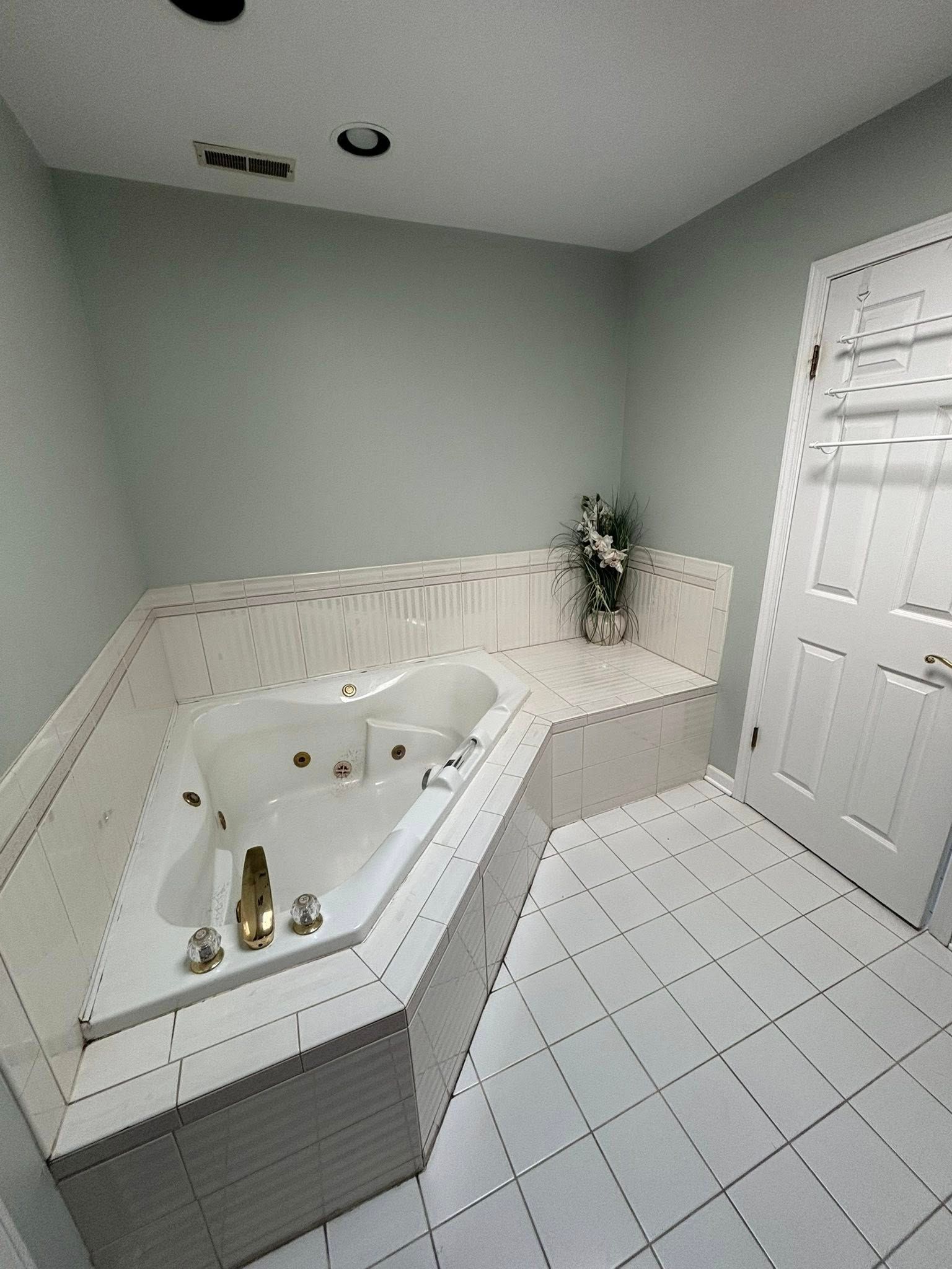 Bathroom with white tiled floors and tub, pale green walls, and a white door.