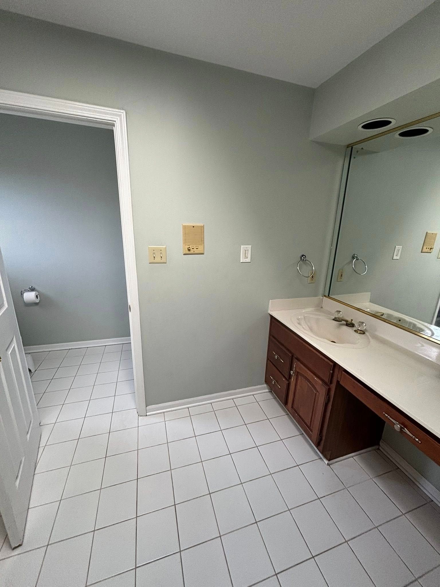 Bathroom with white tile floor, toilet visible, vanity with mirror and lights, light green walls.