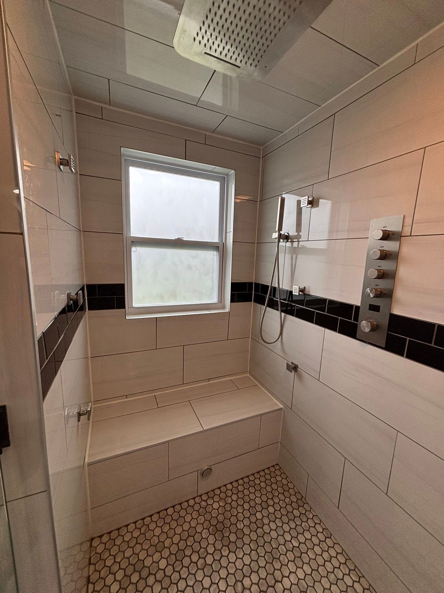 Shower stall with tiled walls, built-in bench, window, and pebble flooring.
