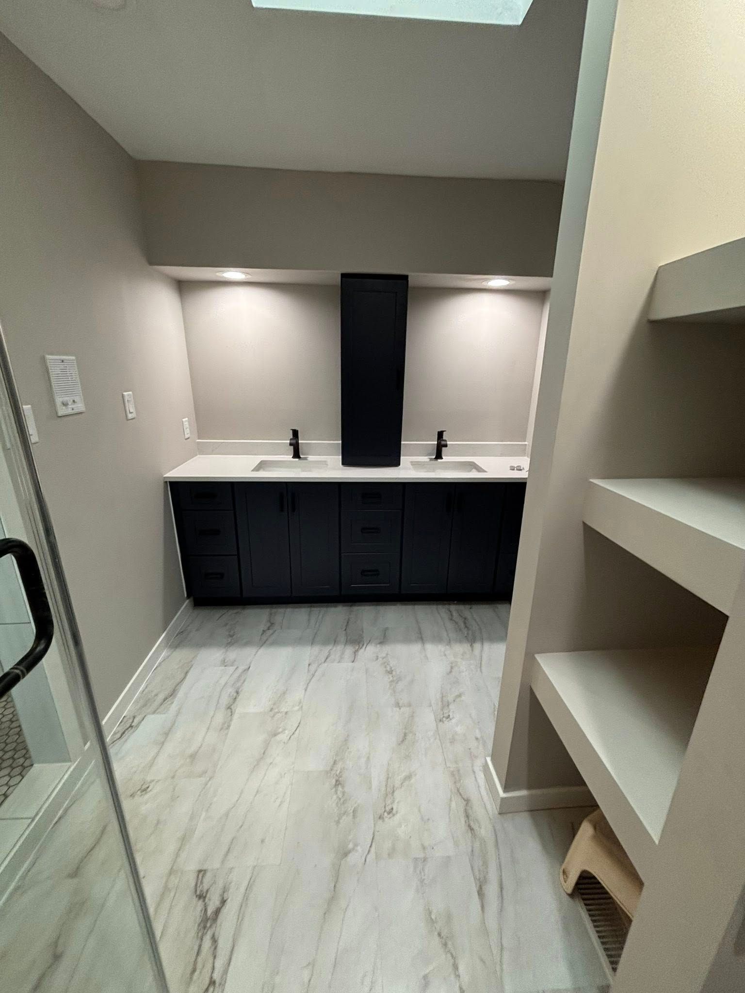 Bathroom with dark blue cabinets, white countertop, and gray and white floor; shelving on the right.