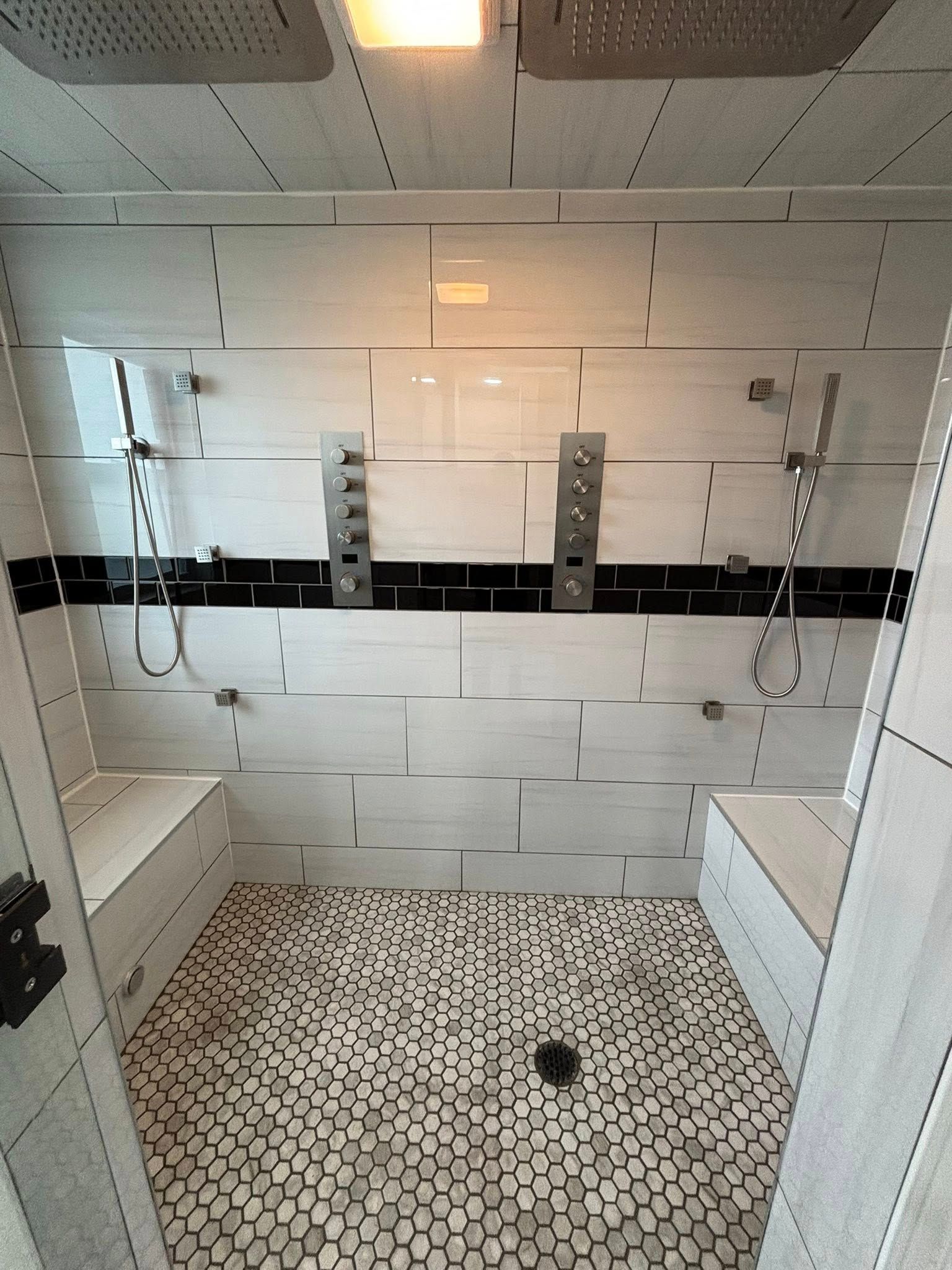 Modern shower with white tiled walls, black accent stripe, built-in benches, and patterned floor.
